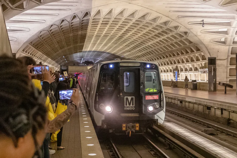Metrorail train pulling into newly opened subterranean station in Washington, D.C. with crowd on platform taking photos.